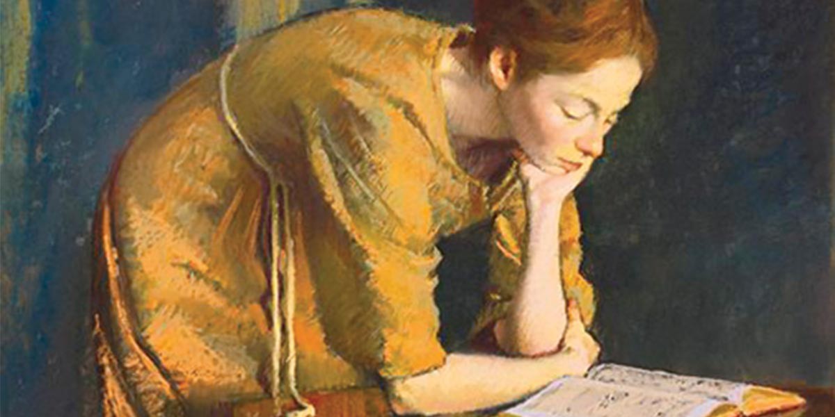 Woman in a mustard-colored dress leaning on her arm, reading a book intently.
