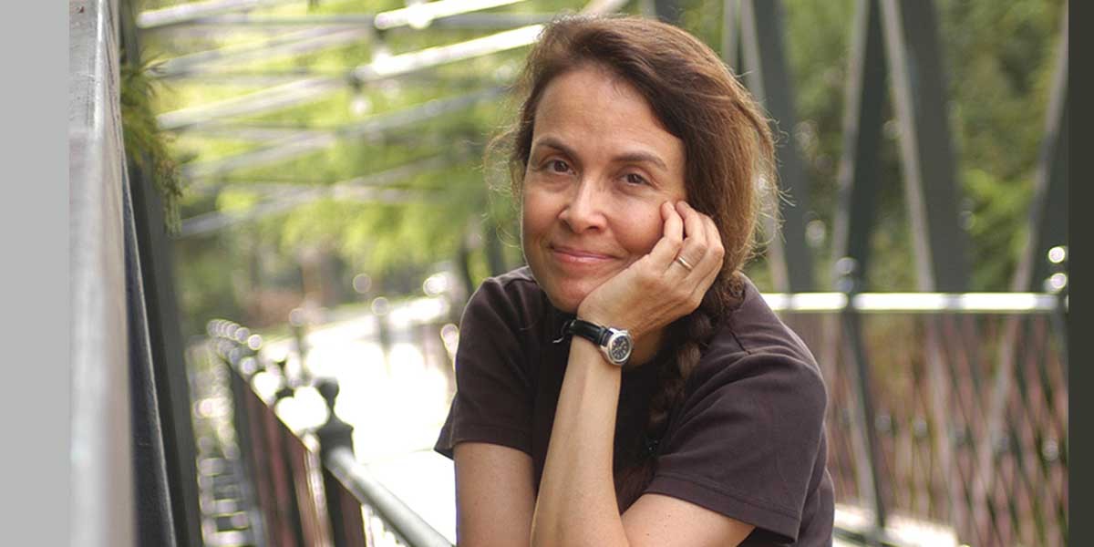 Woman with braided hair leaning on her hand while sitting outdoors by a metal railing.
