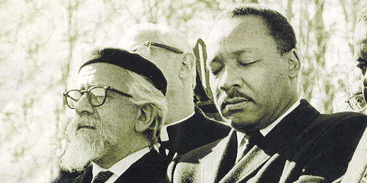 Black and white photo of two men in suits with eyes closed, part of a group in an outdoor setting.