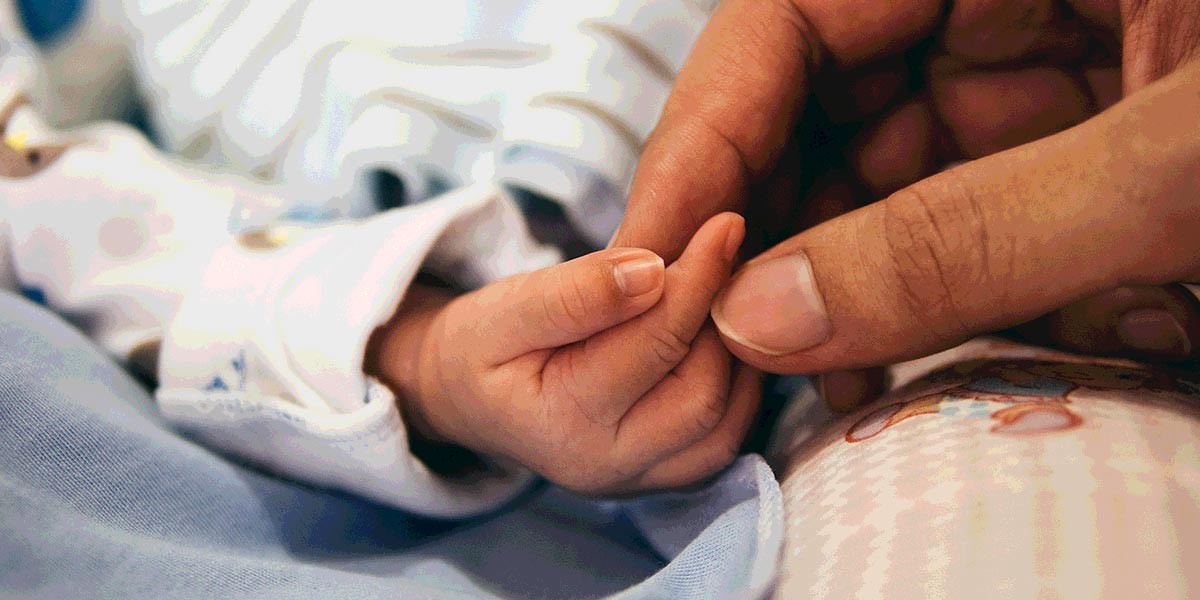 Adult hand gently holding a newborn baby's tiny hand wrapped in soft cloth.
