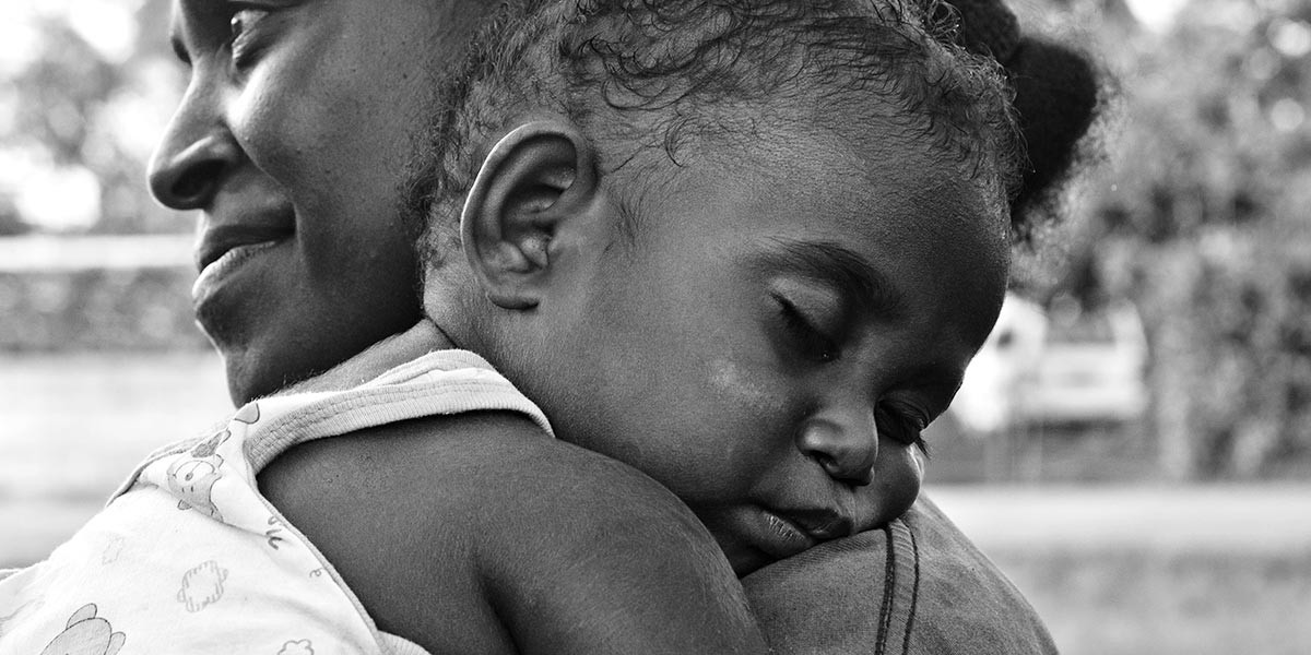 Black and white close-up of a woman holding a sleeping baby resting head on her shoulder.
