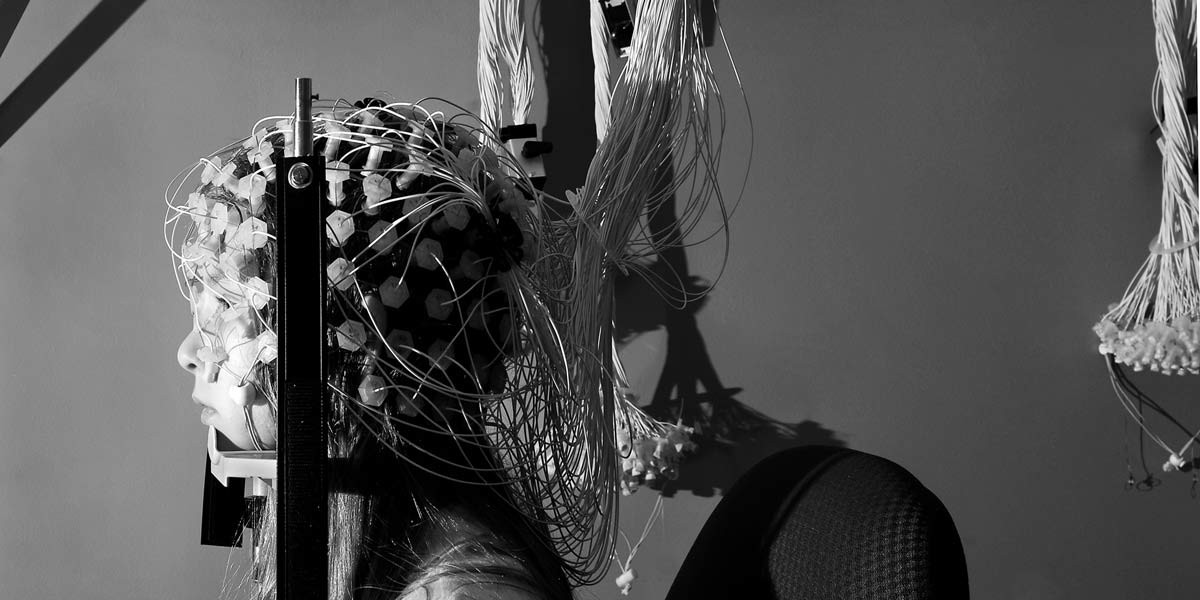 Person wearing a brain-computer interface cap with wired sensors attached to their head.