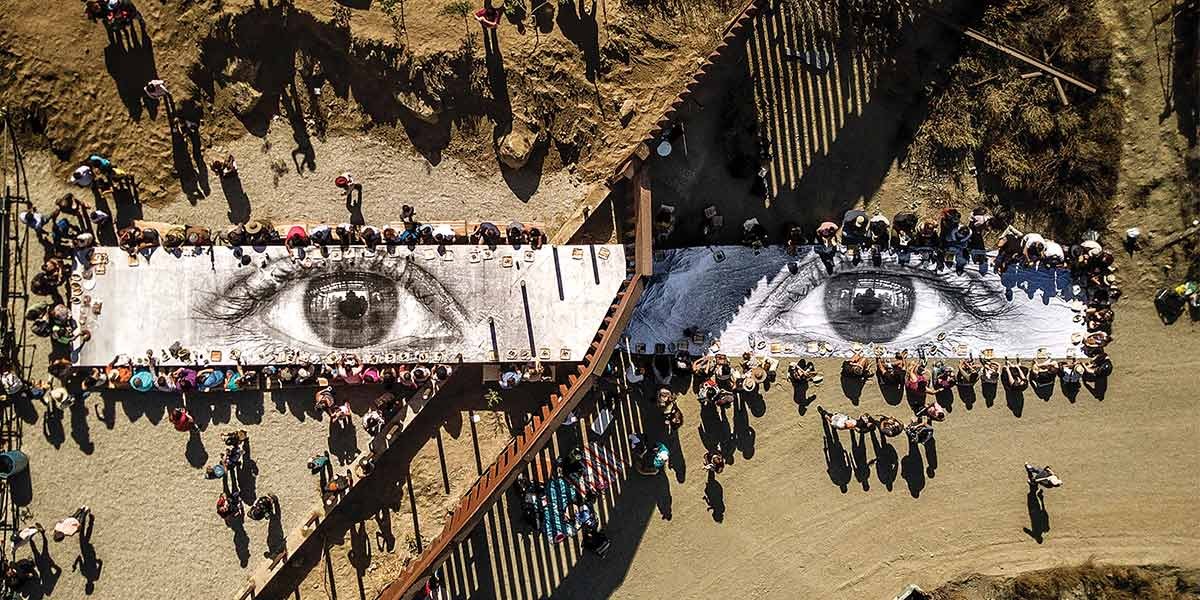 Aerial view of people gathered around two long tables with large black-and-white eyes painted on them.