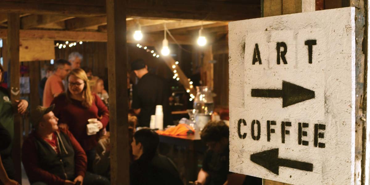 Rustic indoor space with people socializing and a sign pointing right for art and left for coffee.