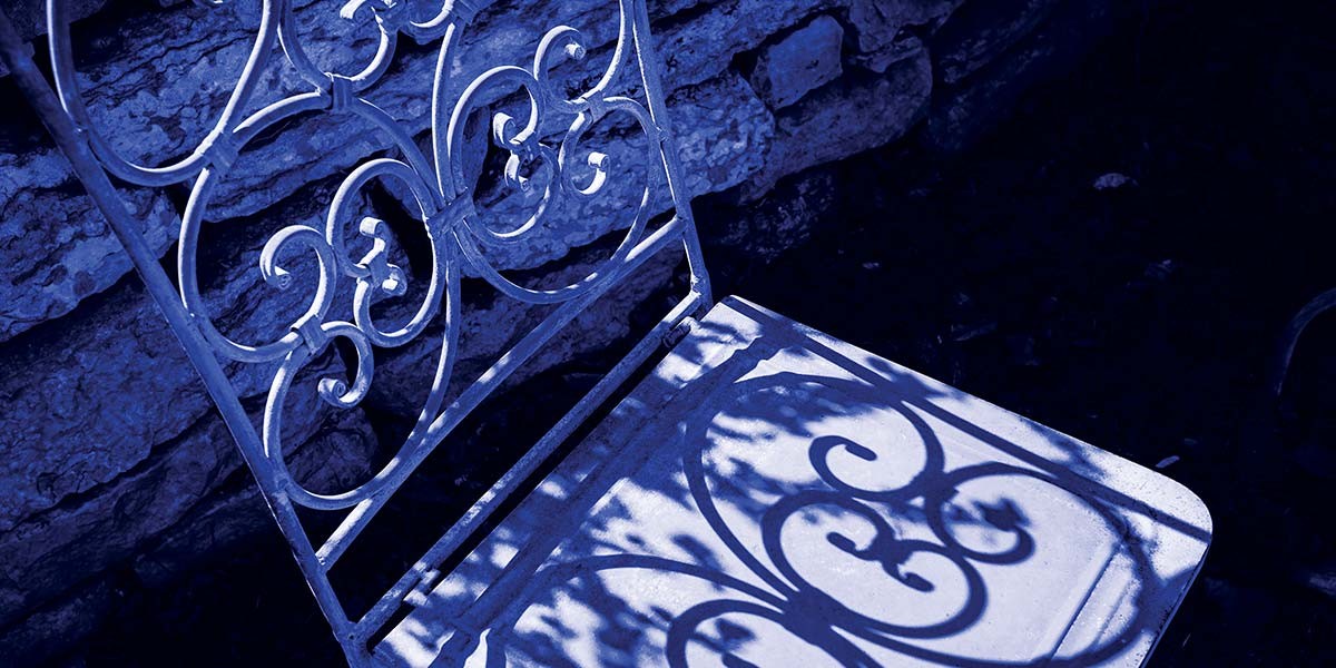 Metal chair casting intricate shadows on its seat against a stone wall background.