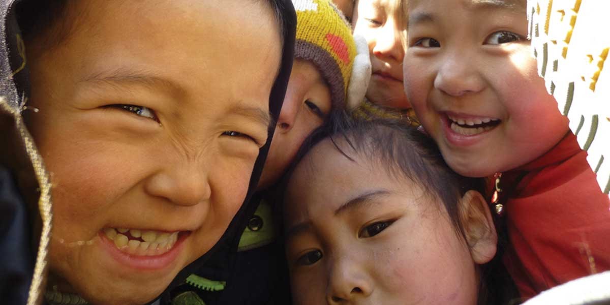 Close-up of five children smiling and making faces closely together outdoors.
