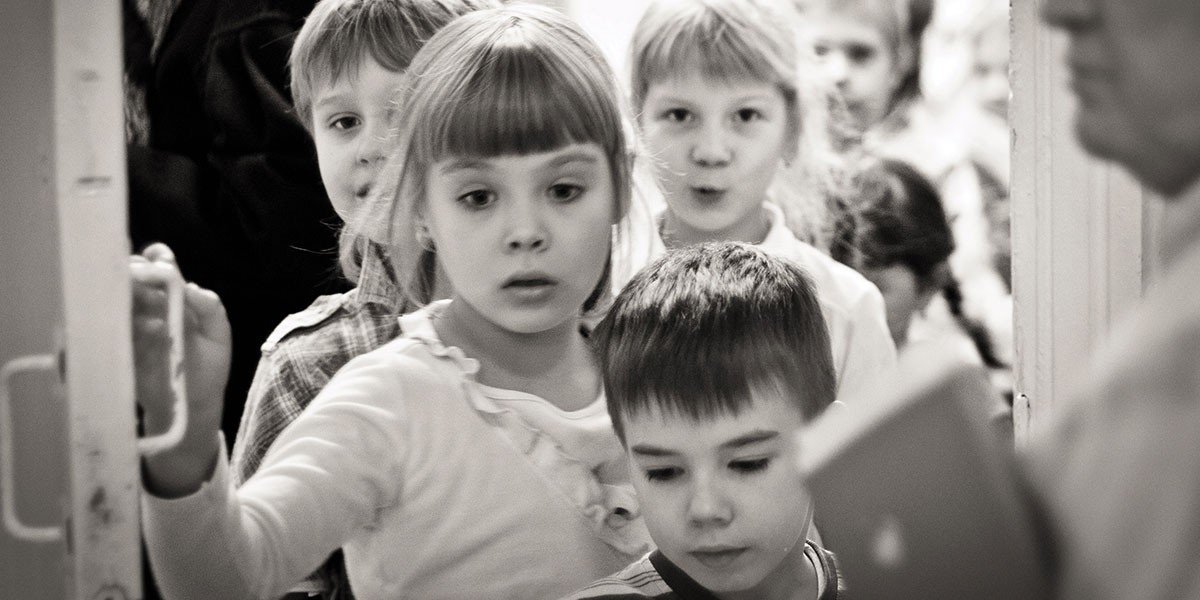 Group of children standing closely together in a narrow hallway near a door.