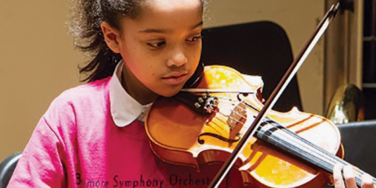Young girl in a pink shirt playing a violin indoors with focus and concentration.