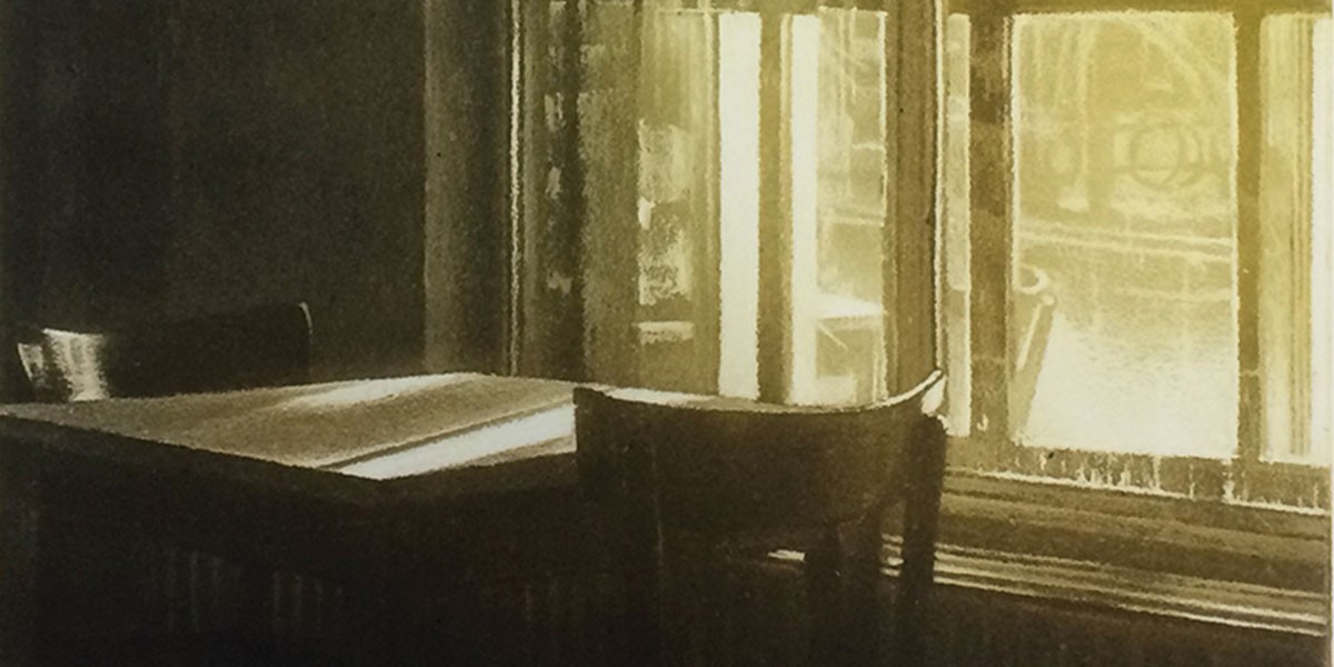 Sunlight filters through a window onto a wooden table and chairs in a dim room.