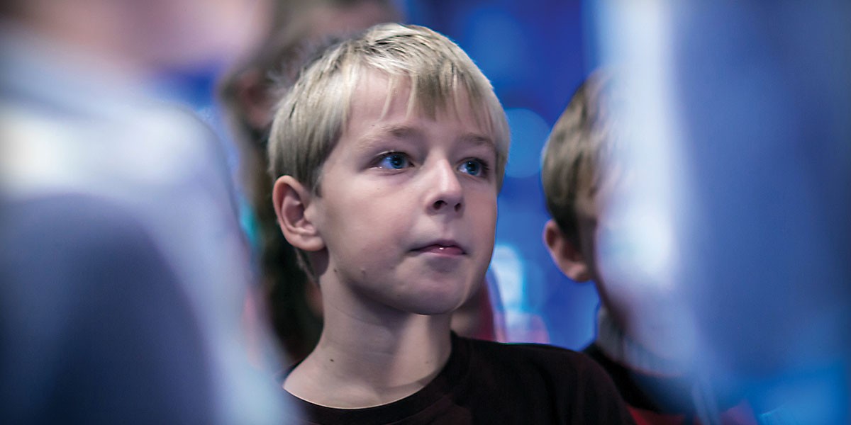 Close-up of a blond boy with blue eyes looking intently ahead in a softly lit setting.