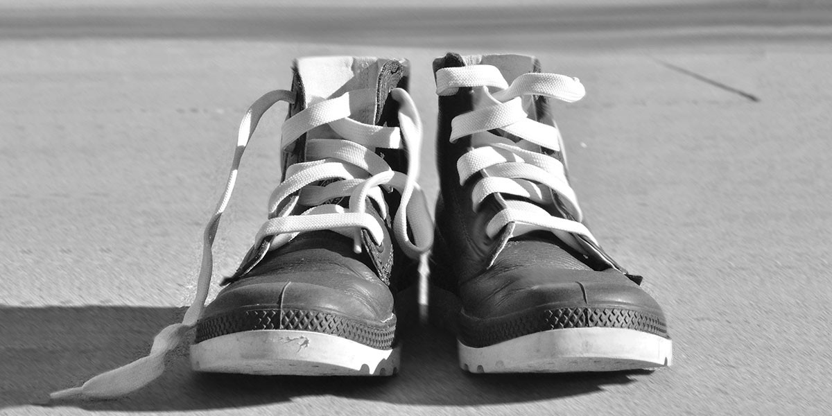 Pair of black high-top sneakers with white laces on a concrete surface casting shadows.