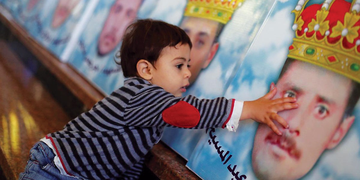Young boy touching a large poster of a man wearing a golden crown with Arabic text.