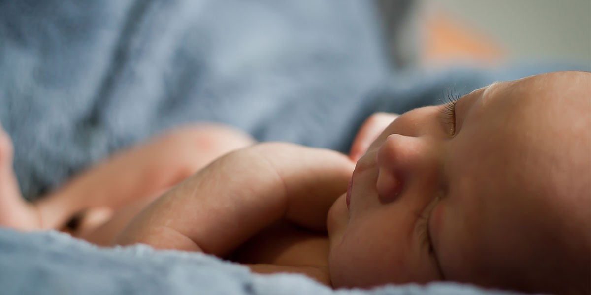 Close-up of a peacefully sleeping newborn baby lying on a soft blue blanket.