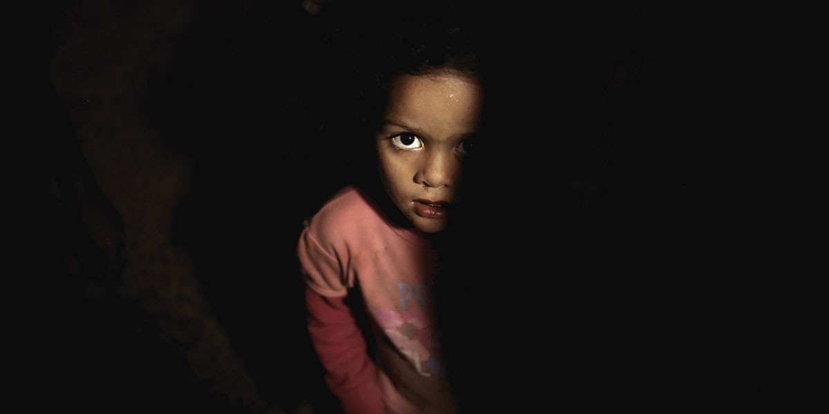 Child in pink shirt looking up with half the face illuminated and the rest in darkness.