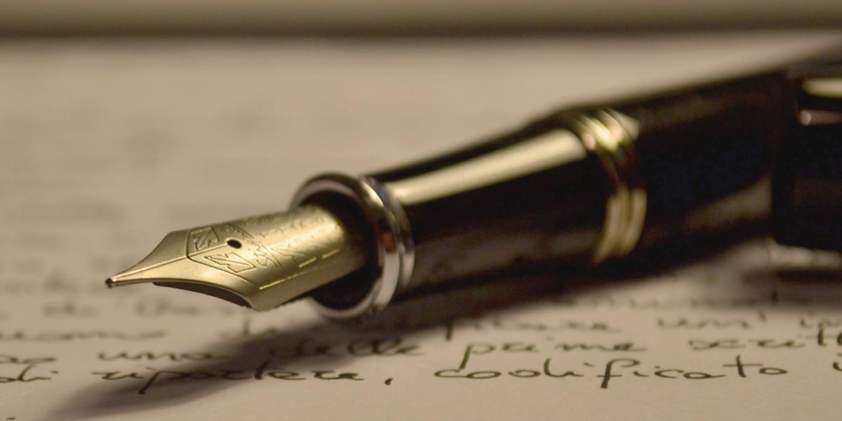 Close-up of a gold-tipped fountain pen resting on handwritten text on paper.
