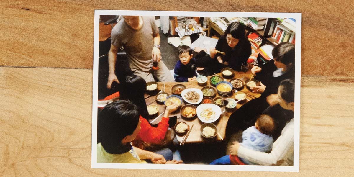 Family seated around a low table eating a meal with various dishes and chopsticks.