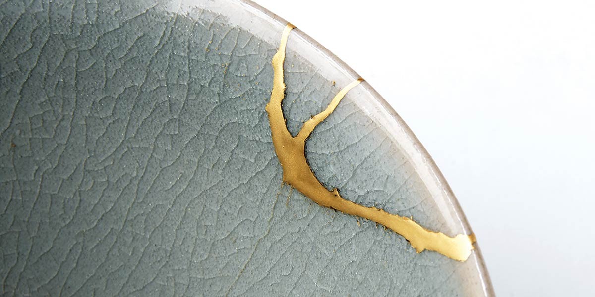 Close-up of a ceramic plate with a wide crack repaired using gold in a kintsugi style.