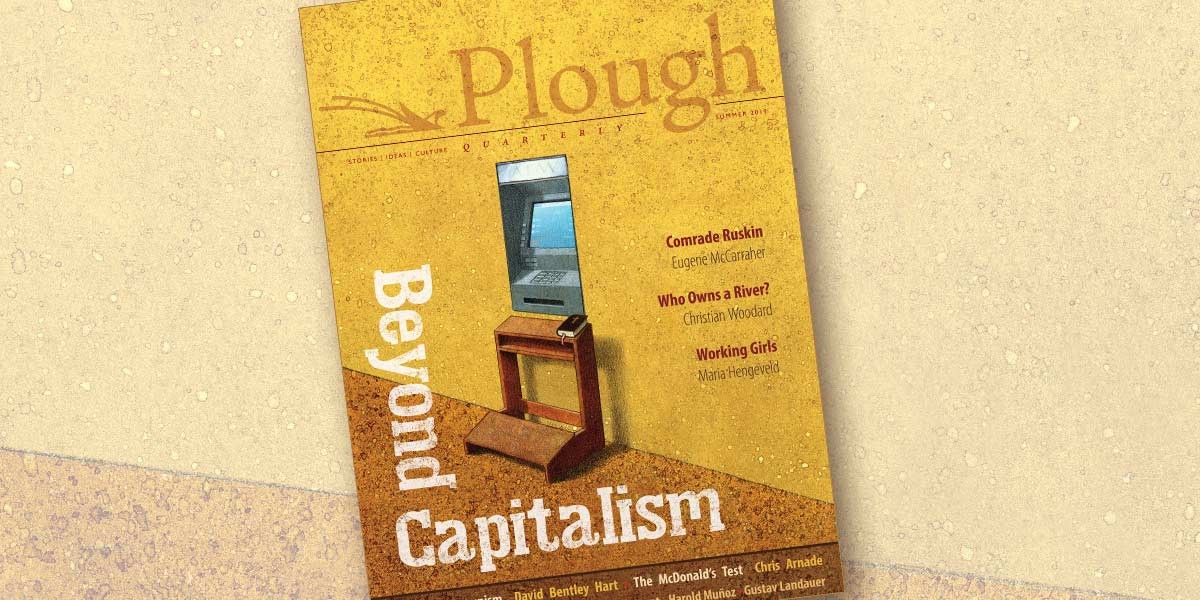 Magazine cover titled Plough Quarterly with theme Beyond Capitalism and a computer on a wooden desk.