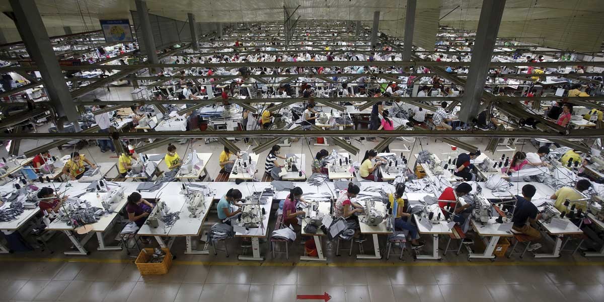 Workers seated in rows operating sewing machines in a large garment factory.