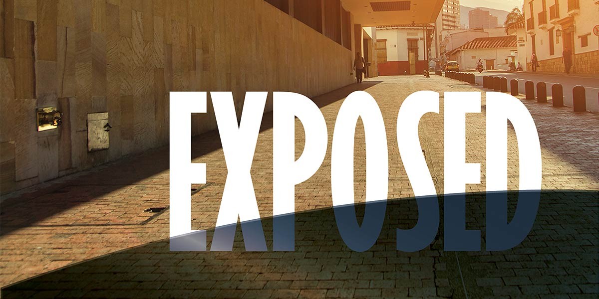 Street scene with large text 'EXPOSED' casting a shadow on a brick-paved road.