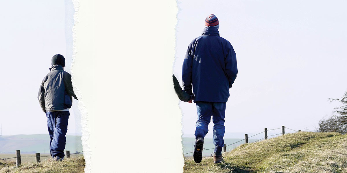 Two people walking outdoors in cold weather on grassy terrain with a torn paper effect between them.