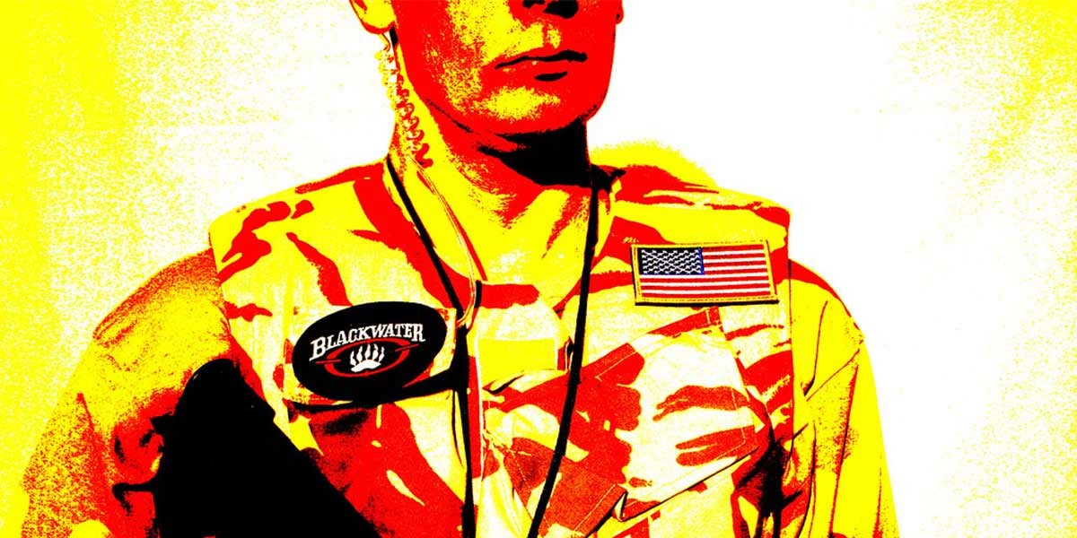 Close-up of a person in camouflage gear with a Blackwater patch and a U.S. flag patch on the chest.