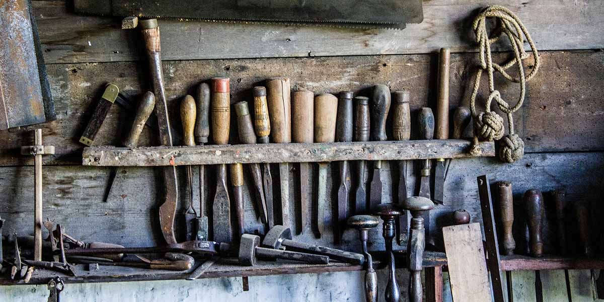 Vintage woodworking tools with wooden handles hanging on a weathered wooden wall with coiled rope.