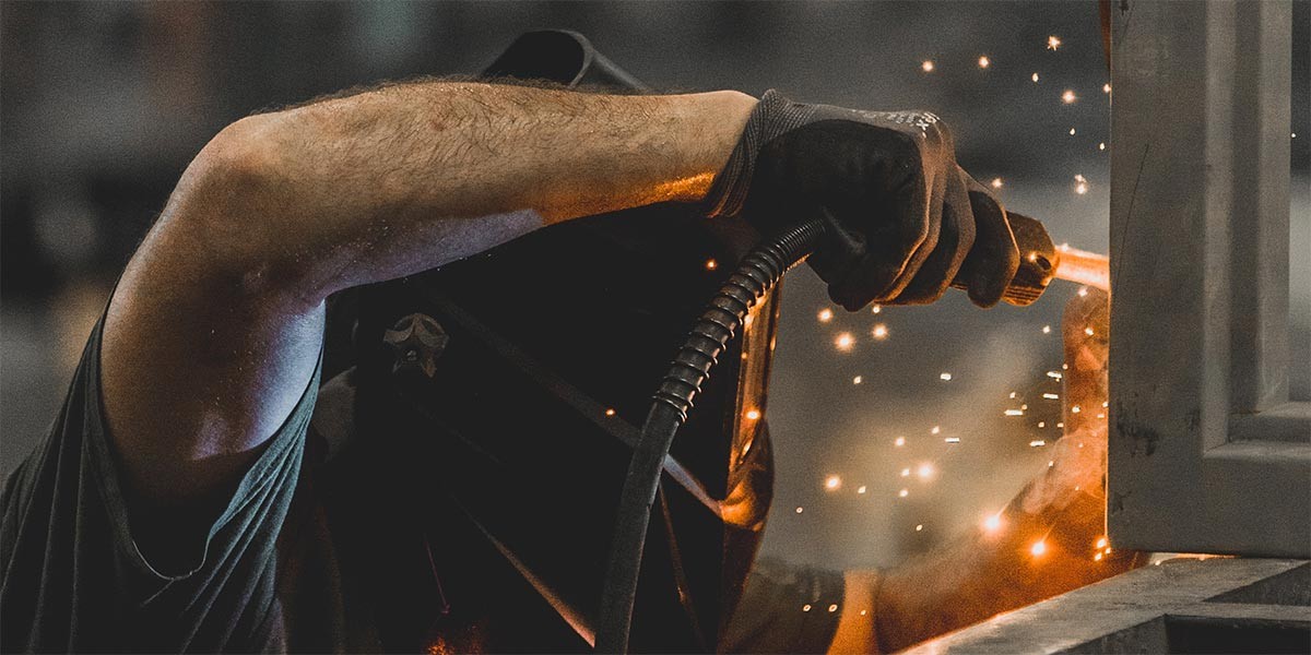 Welder wearing protective gloves and mask, welding metal with sparks flying.