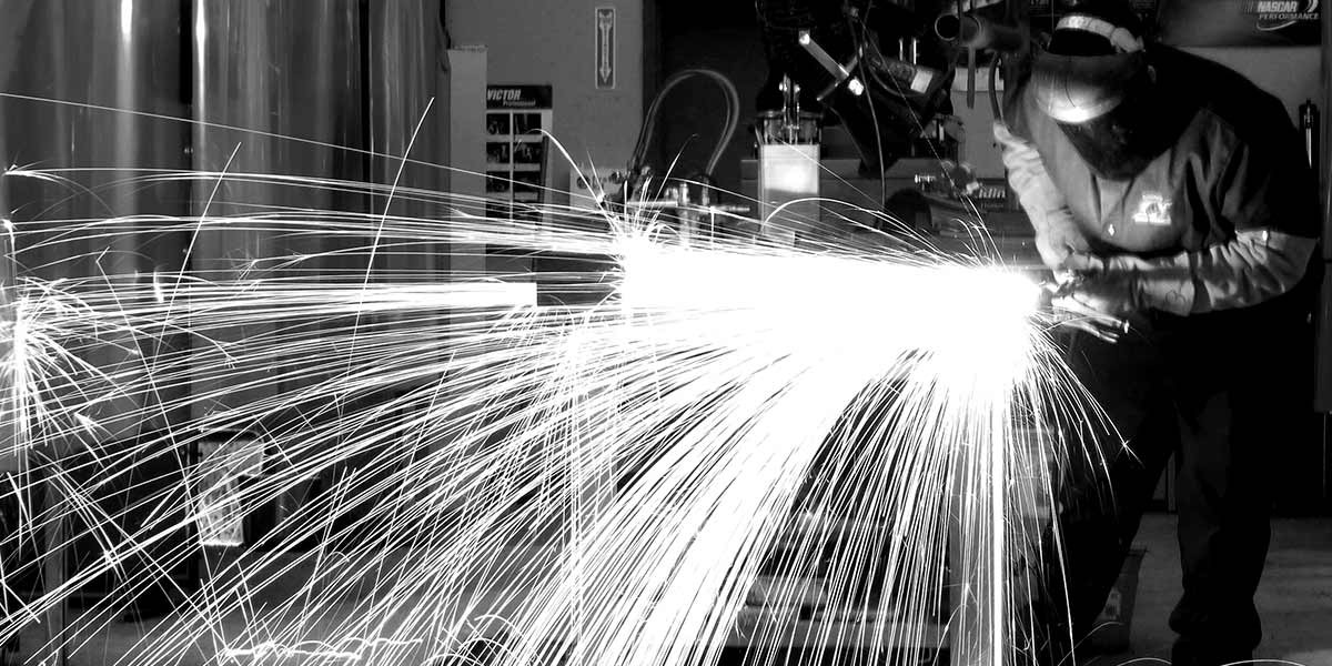 Welder in protective gear using a torch, creating bright sparks in a workshop.