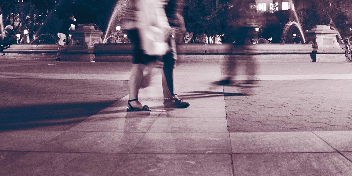 Blurred motion of people walking near a fountain in a nighttime urban square.