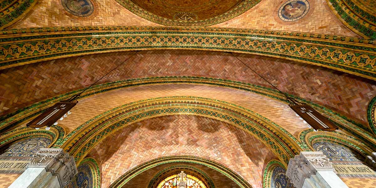 Arched ceiling with detailed green and gold tile patterns and brickwork in a grand historic building.
