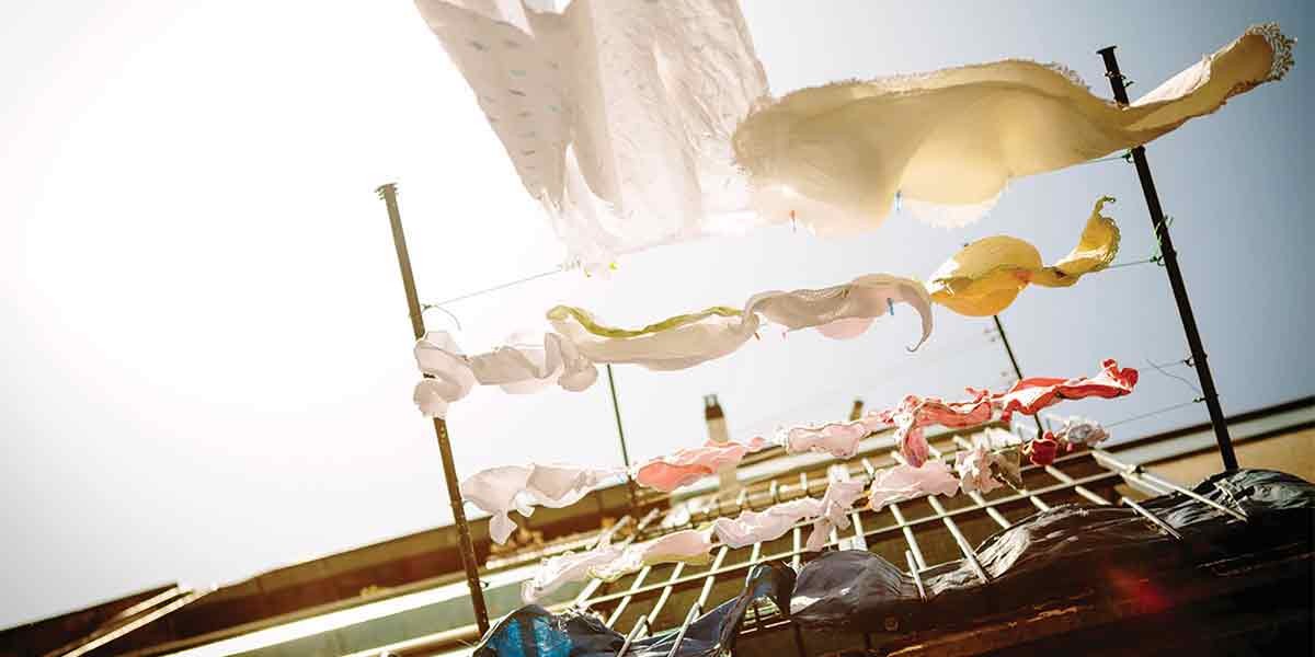 Colorful fabric pieces hanging on lines drying outdoors against a bright sunny sky.