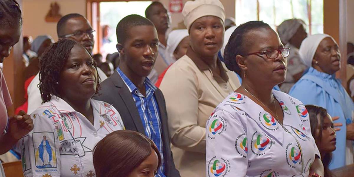 Group of people attentively participating in an indoor event or gathering, some in uniform or traditional attire.