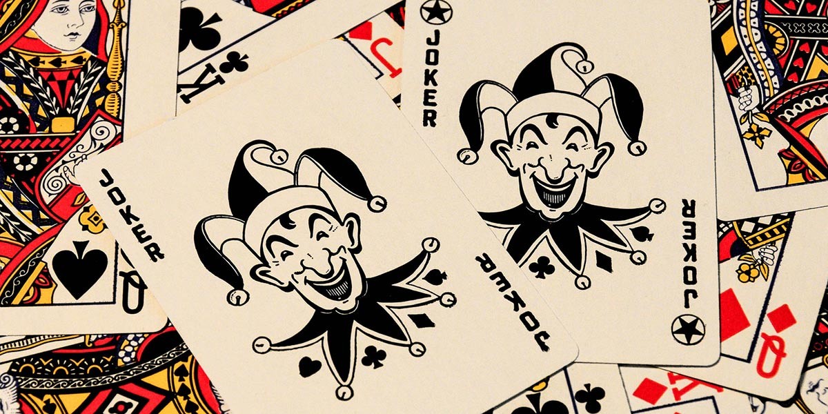 Two black and white joker playing cards on top of various colorful face cards.