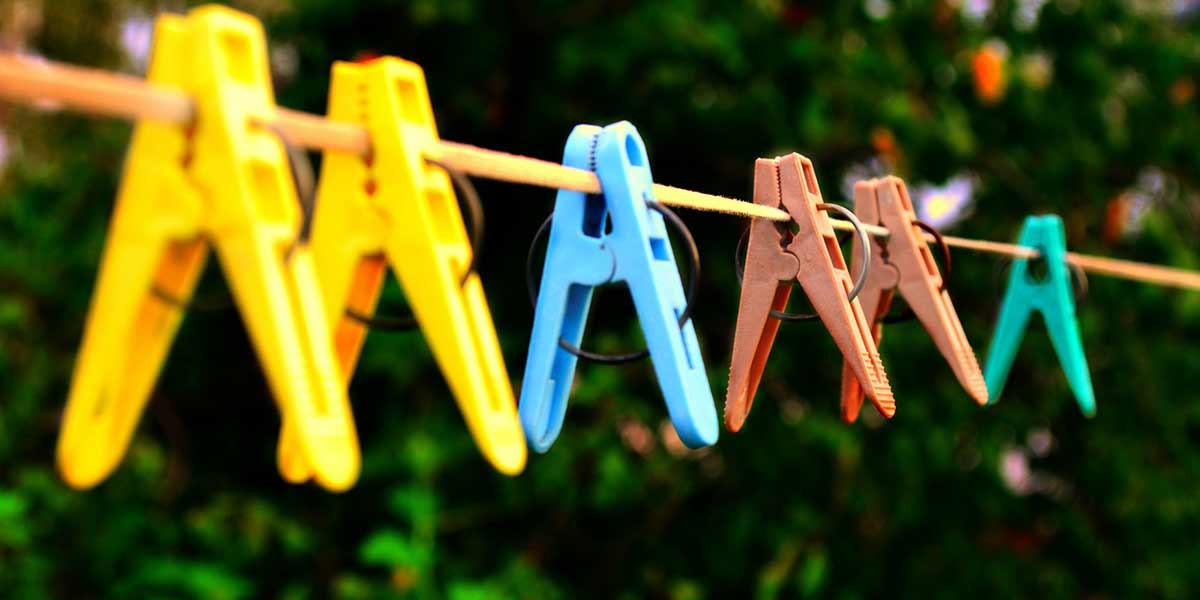 Yellow, blue, brown, and teal clothespins clipped on a clothesline against a blurred natural background.