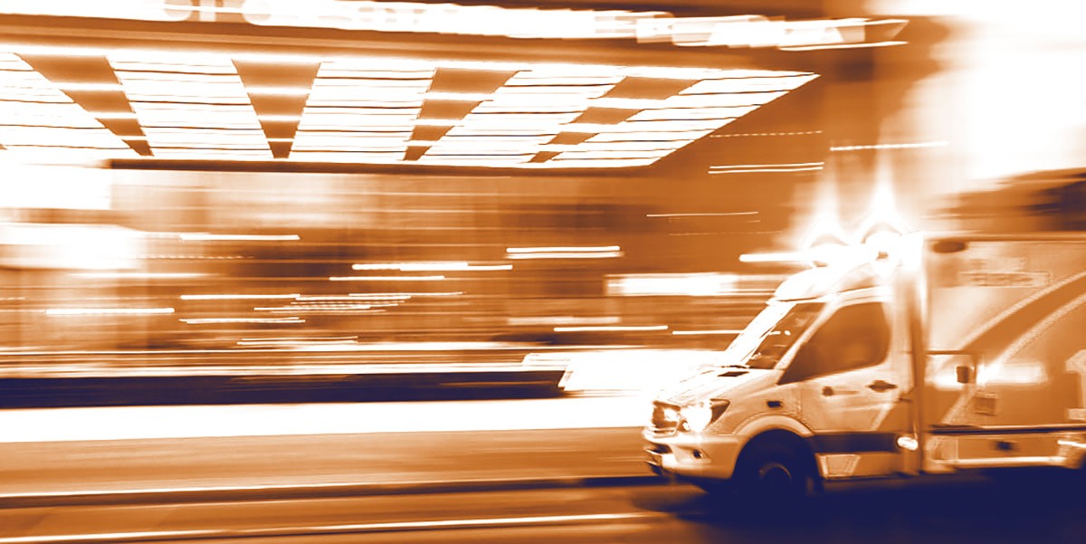 Emergency ambulance with flashing lights speeding on street at night with blurred lights.