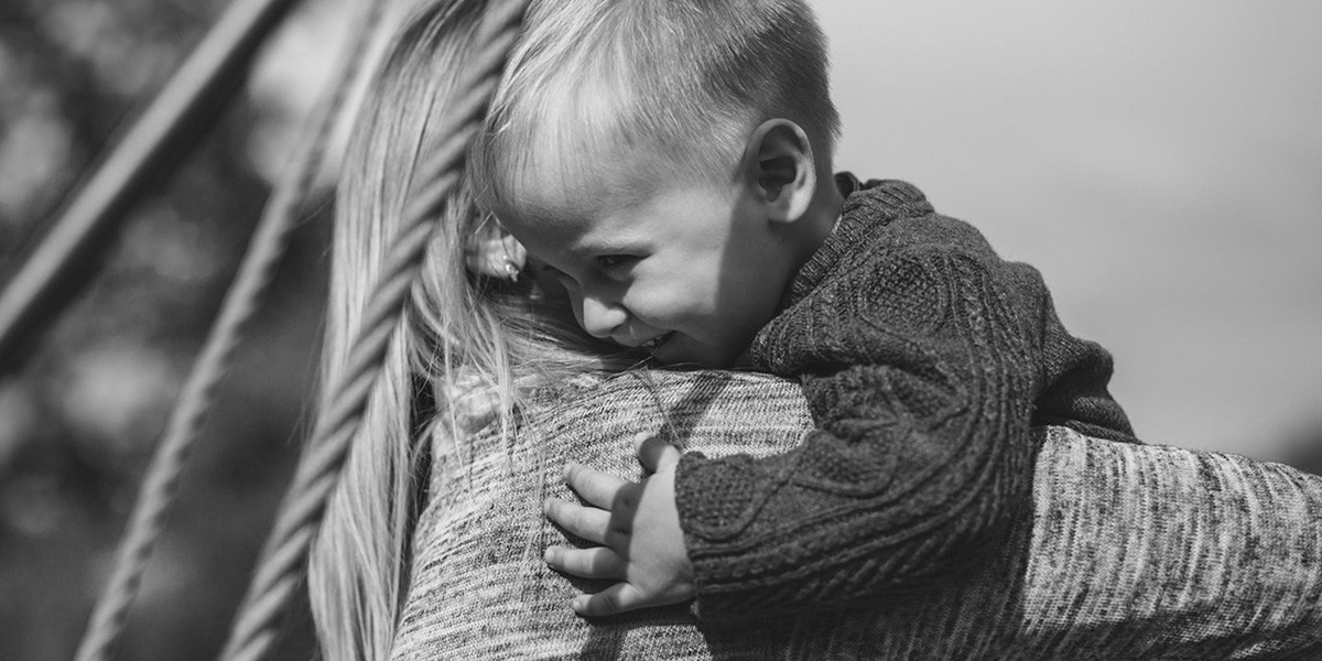 Child with short hair hugging an adult in a sweater on a swing, black and white photo.