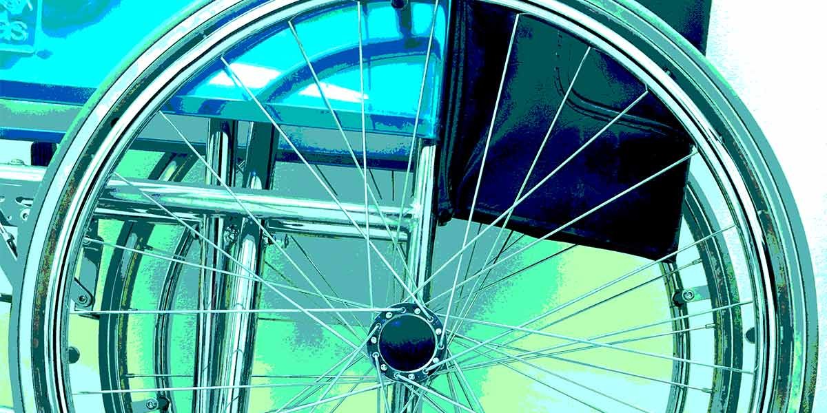 Close-up of a wheelchair wheel with metal spokes and part of the seat visible.