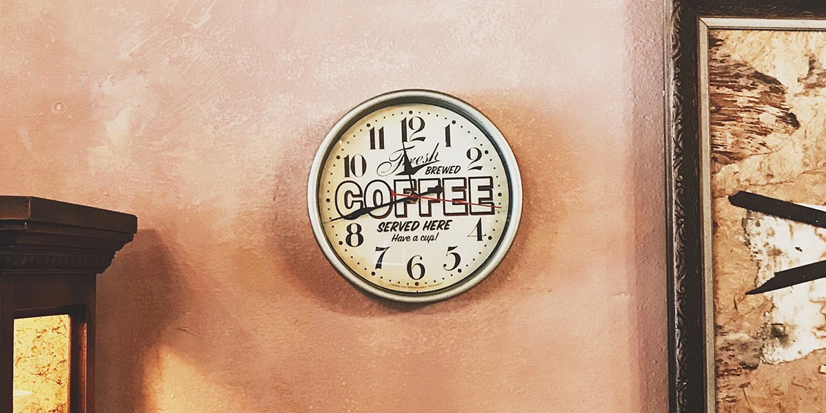 Wall clock with the text 'Fresh brewed coffee served here Have a cup!' on a pinkish wall.