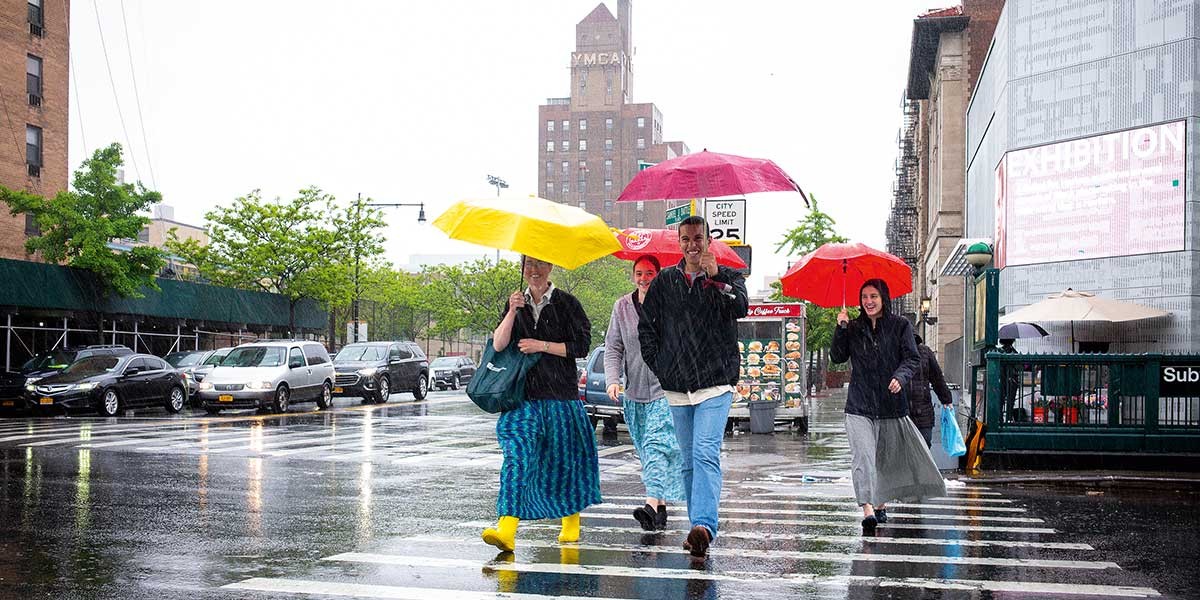 Four people crossing a rainy city street holding colorful umbrellas, including red and yellow.