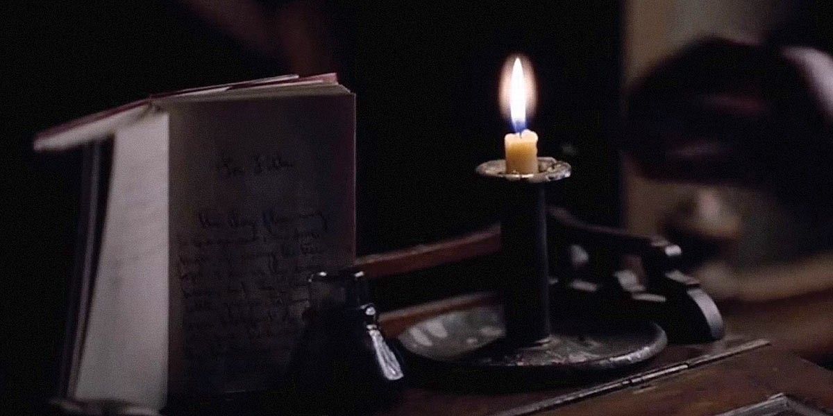 Open handwritten book beside a lit candle on a dark wooden table.