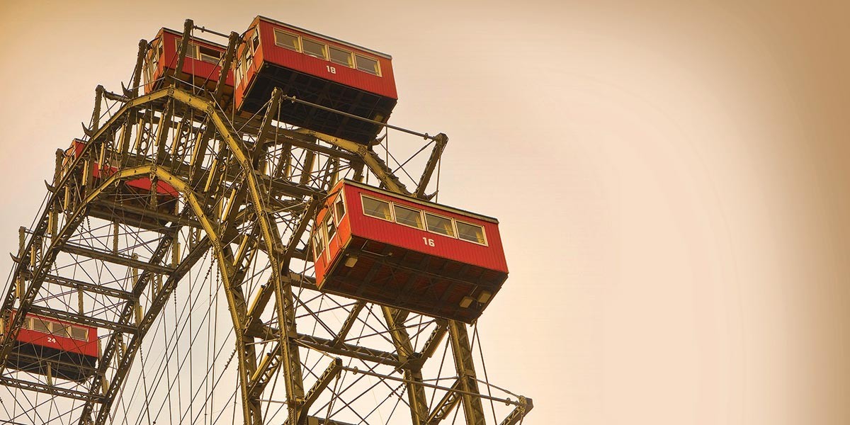 Vintage-style Ferris wheel with red box-shaped cabins against a beige sky.