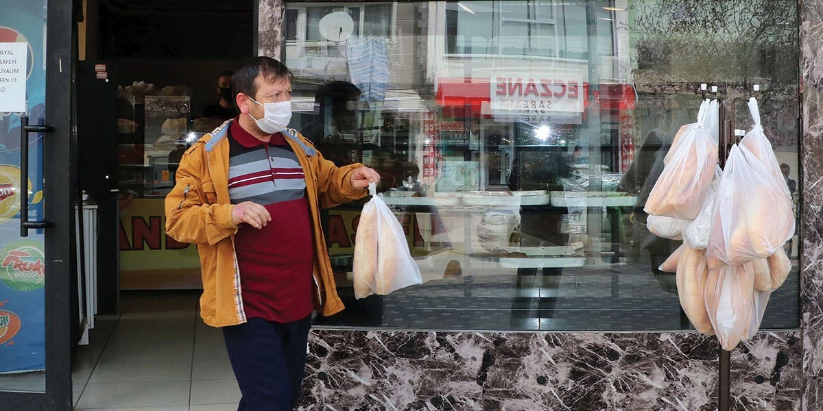 Man wearing a face mask holding a bag of bread outside a shop with bread loaves hanging on the door.