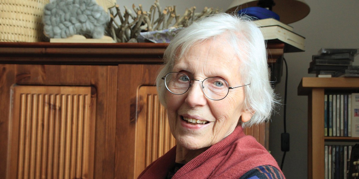 Smiling elderly woman with white hair and glasses wearing a red shawl in a cozy room.