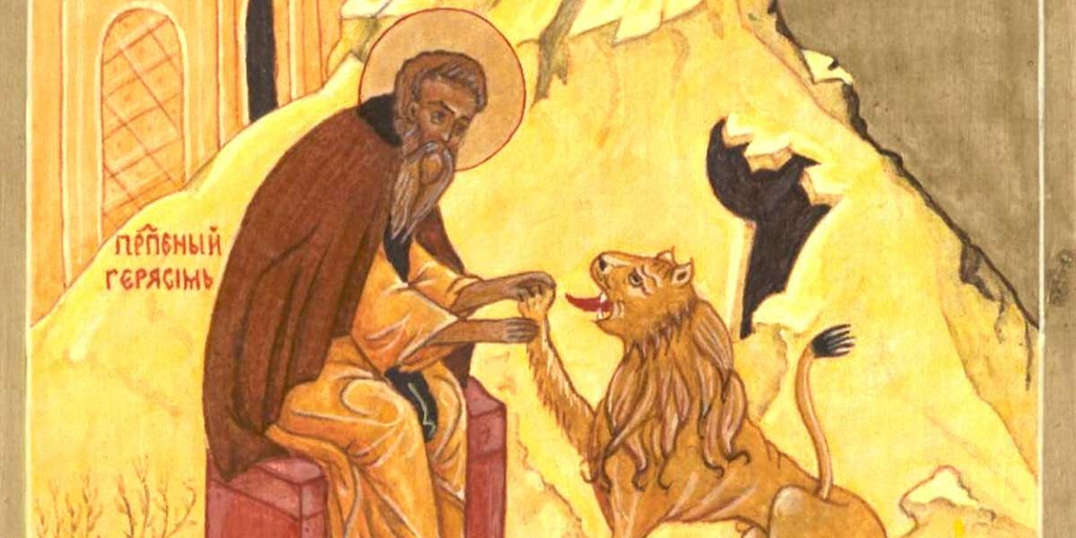 A bearded saint with a halo sits holding a lion's paw inside a cave-like setting.