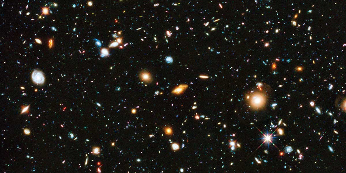 Deep space view showing numerous distant galaxies and stars scattered across a dark background.