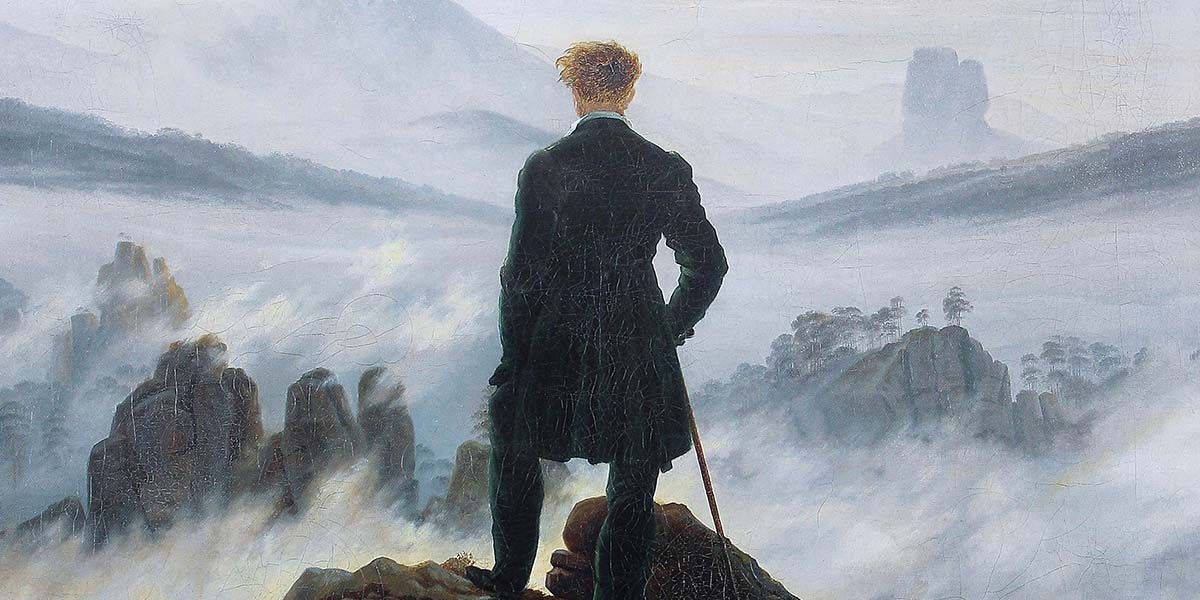 Man in black coat standing on rocky cliff, gazing at misty mountains and foggy landscape.