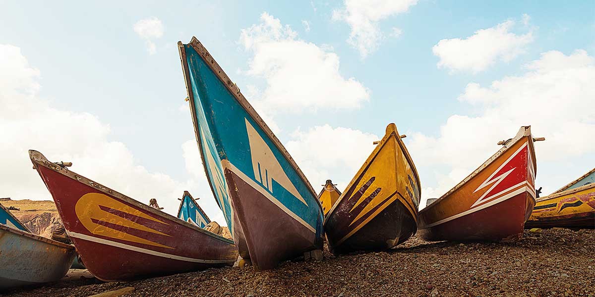 Colorful wooden boats with painted designs resting on a rocky shore under a partly cloudy sky.
