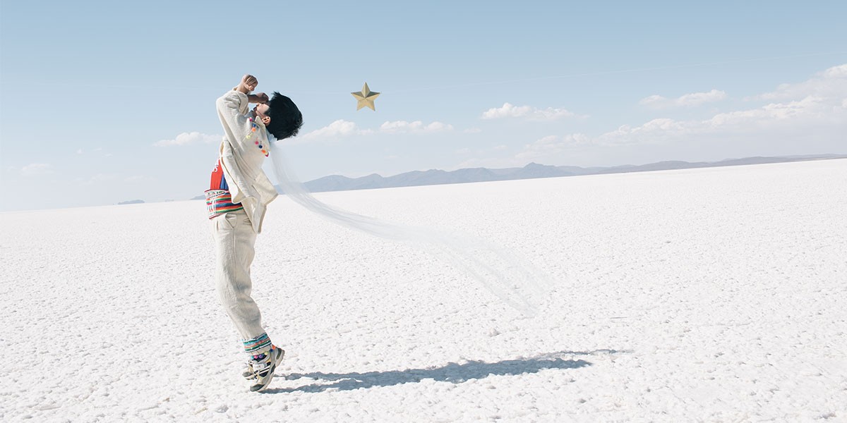 Person jumping on white cracked salt flat with mountains and blue sky in the background.