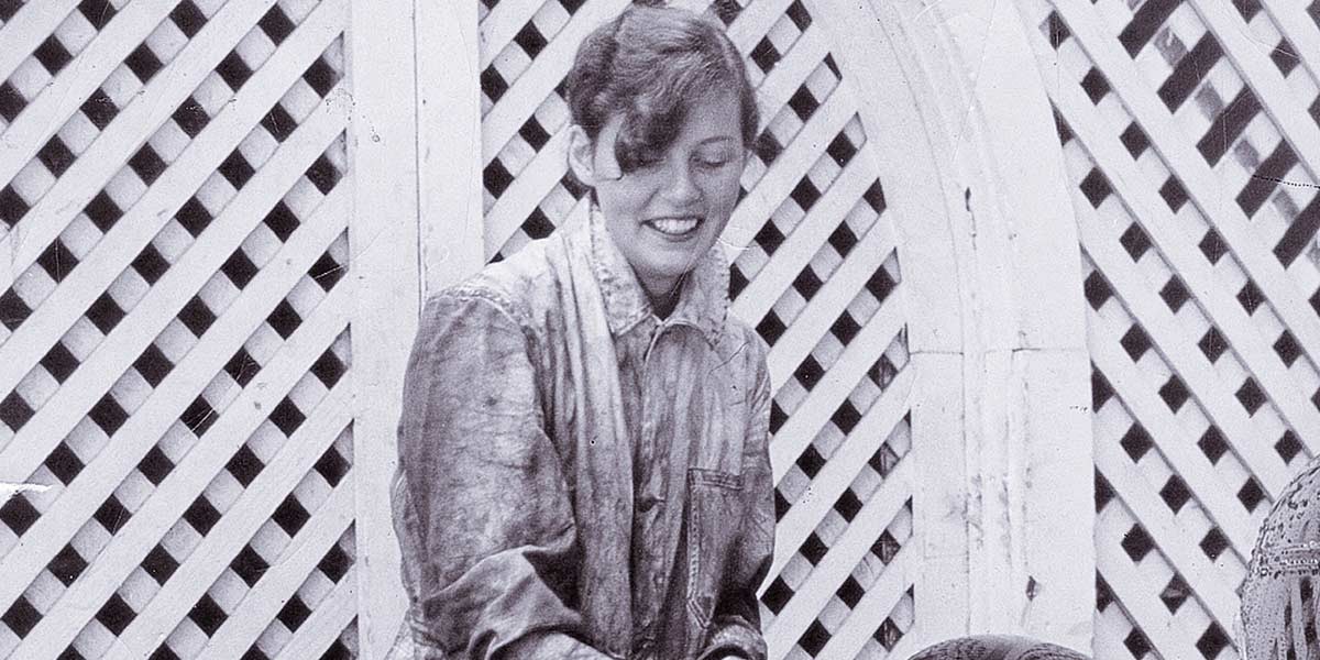 Black and white image of a smiling woman in a jacket against a lattice background.
